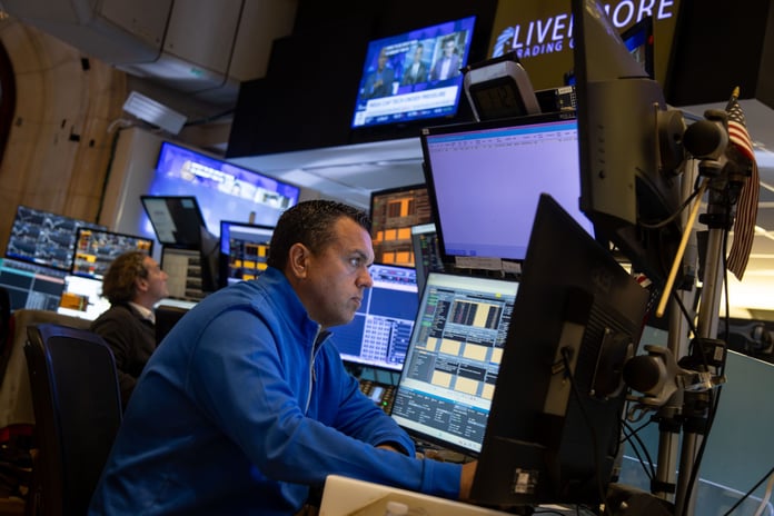 S&P 500 futures today: a trader works at a multi-screen dealing desk beneath a television carrying a megacap technology headline