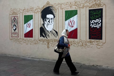 A woman walks past a Tehran wall painted with Iranian flags and a mural of the supreme leader