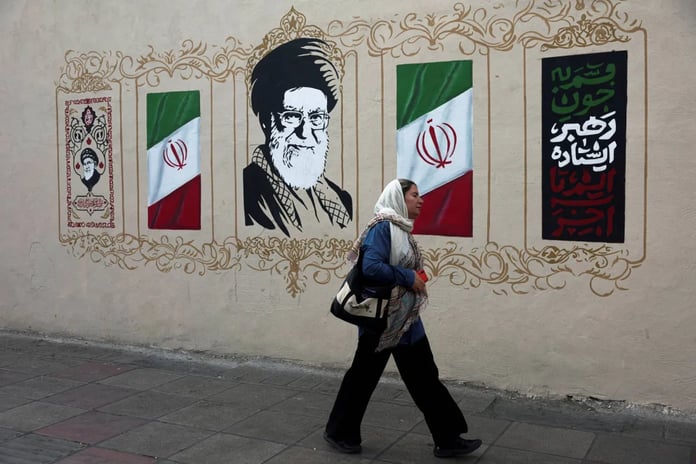 A woman walks past a Tehran wall painted with Iranian flags and a mural of the supreme leader
