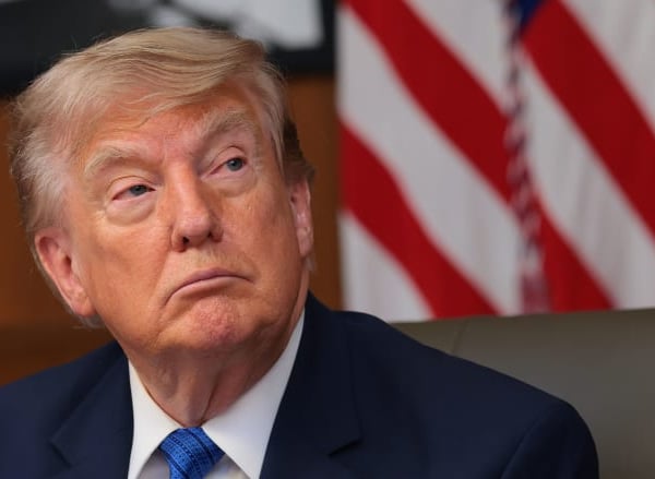 US President Donald Trump seated with American flag in background