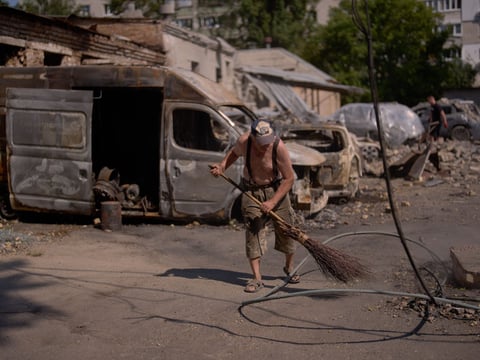 A man sweeps rubble with a besom broom beside burnt-out vans and downed power cables after a strike in Ukraine