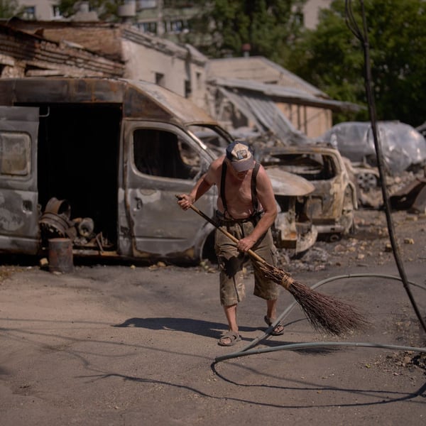 A man sweeps rubble with a besom broom beside burnt-out vans and downed power cables after a strike in Ukraine