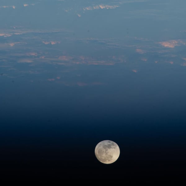 A waxing gibbous moon hanging above the atmospheric limb of Earth over the Pacific Ocean