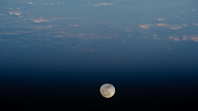 A waxing gibbous moon hanging above the atmospheric limb of Earth over the Pacific Ocean