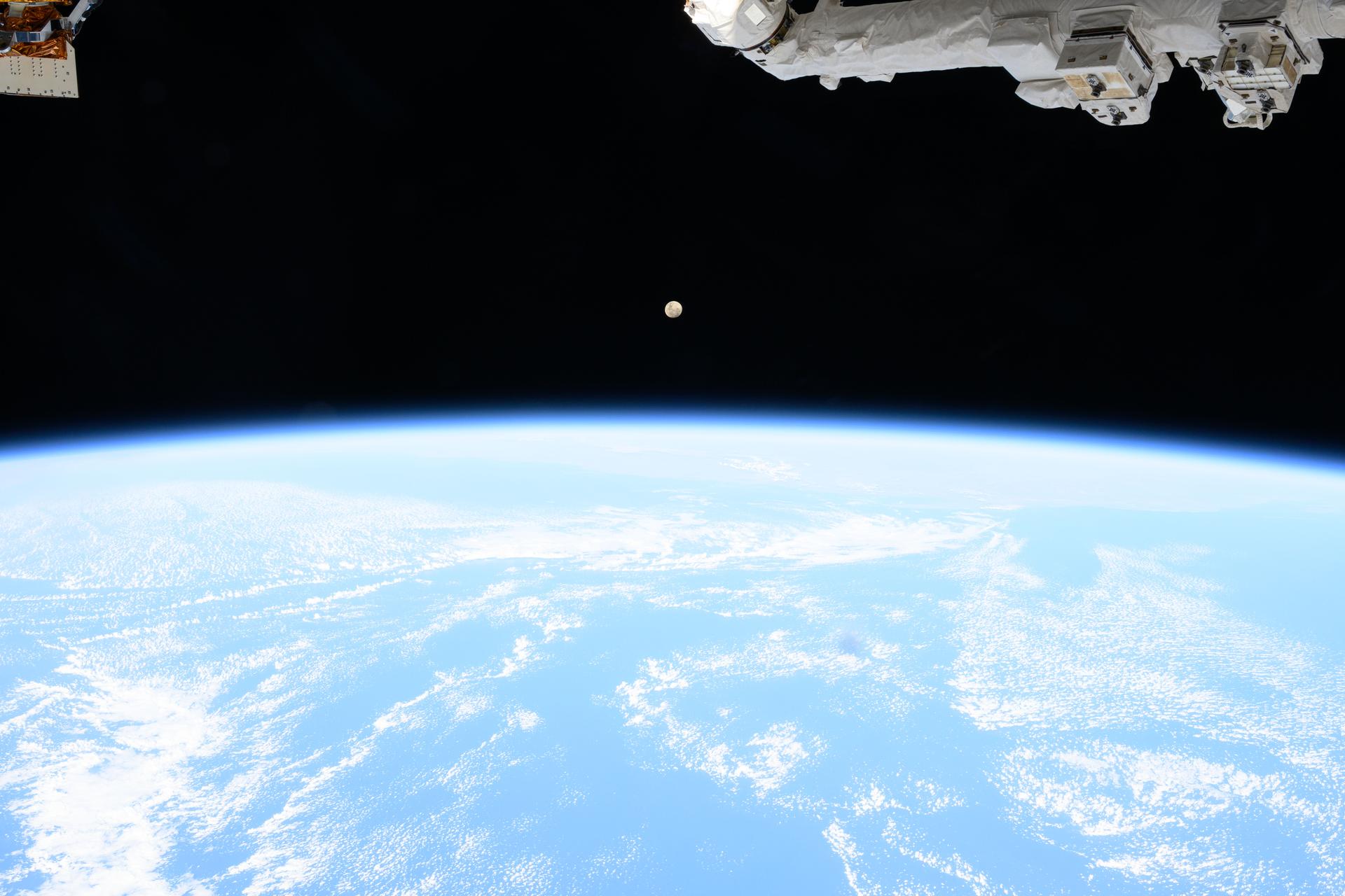 A waxing gibbous moon hangs above the bright curve of Earth's atmosphere in a photograph taken from the International Space Station