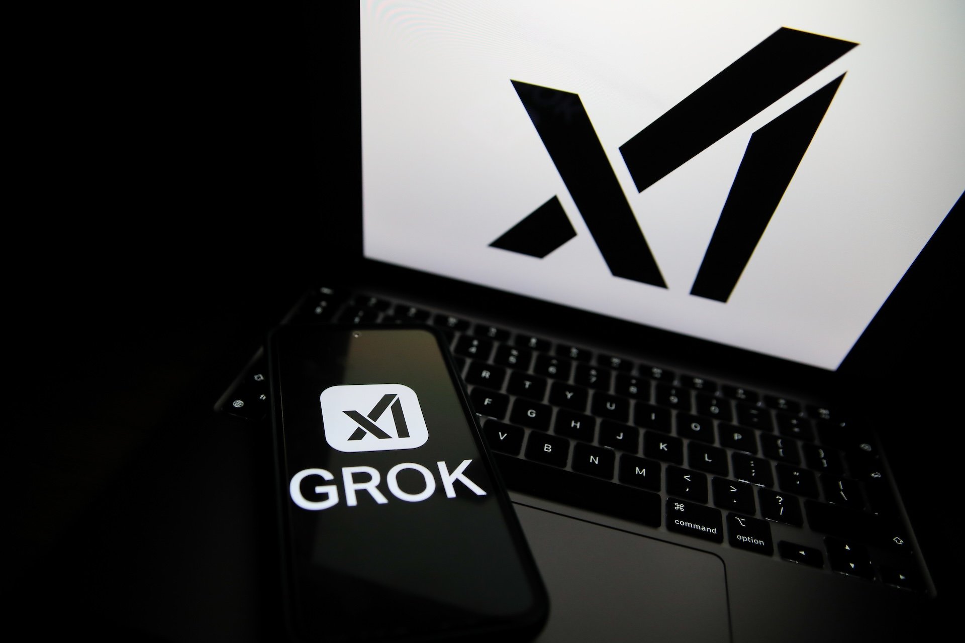 Grok logo displayed on a smartphone next to a laptop showing the xAI logo