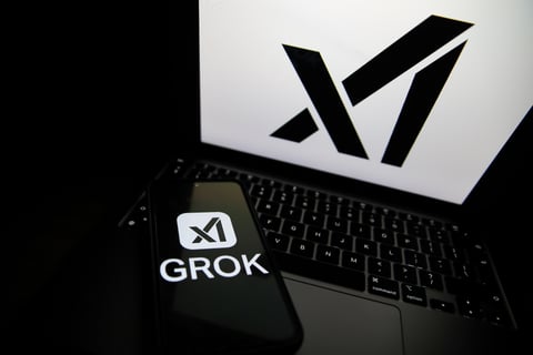 Grok logo displayed on a smartphone next to a laptop showing the xAI logo