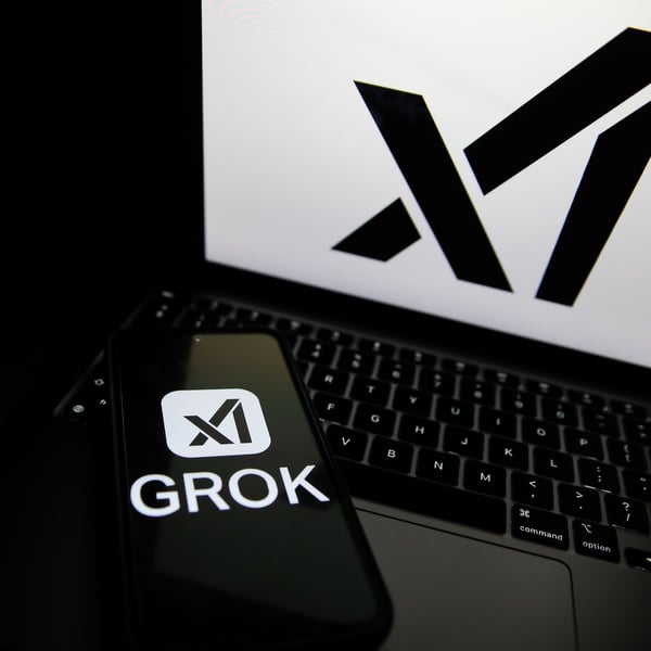 Grok logo displayed on a smartphone next to a laptop showing the xAI logo