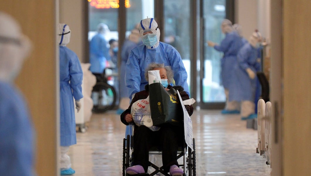 A medical worker in protective gear moves a coronavirus patient in a wheelchair at a hospital in Wuhan, China