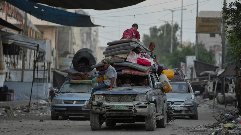 Displaced families push hand-carts with belongings through damaged streets in Gaza City after renewed strikes.