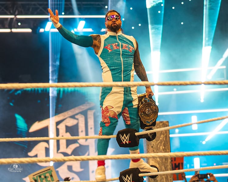 Jey Uso standing on the ring apron in teal and white YEET ring gear and Yeet sunglasses, holding the WWE Intercontinental Championship aloft