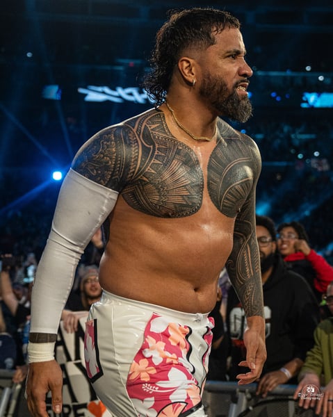 Jey Uso walking through the crowd barrier at the 2025 Royal Rumble in white ring gear with pink hibiscus print, Samoan tattoo work across his chest and both arms