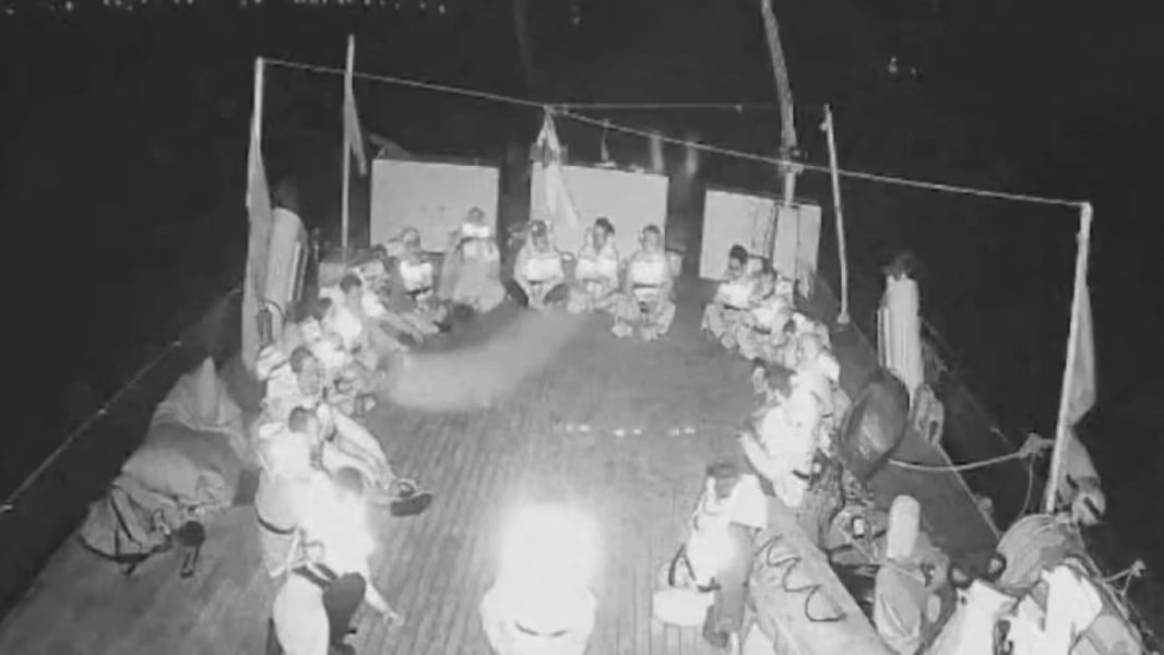 Detained flotilla passengers seated on deck during transfer to Israeli vessels