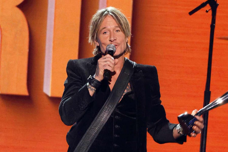 Keith Urban onstage era, tour continues Keith Urban smiling on a red carpet before a performance, guitar focused career image