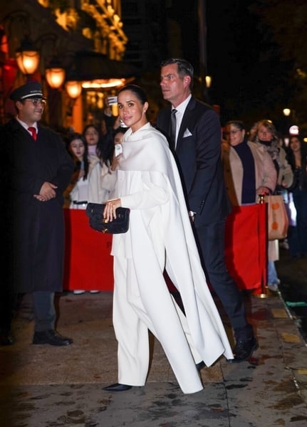 Wide shot of Meghan Markle walking in an all white cape look during Paris Fashion Week 2025.