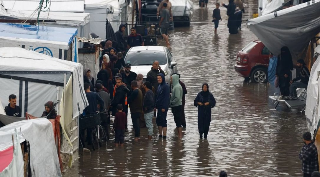 Gaza Children Face Winter Storm Devastation in Flooded Camps Palestinian children stand beside collapsed tents flooded by Storm Byron in Gaza displacement camp December 2025