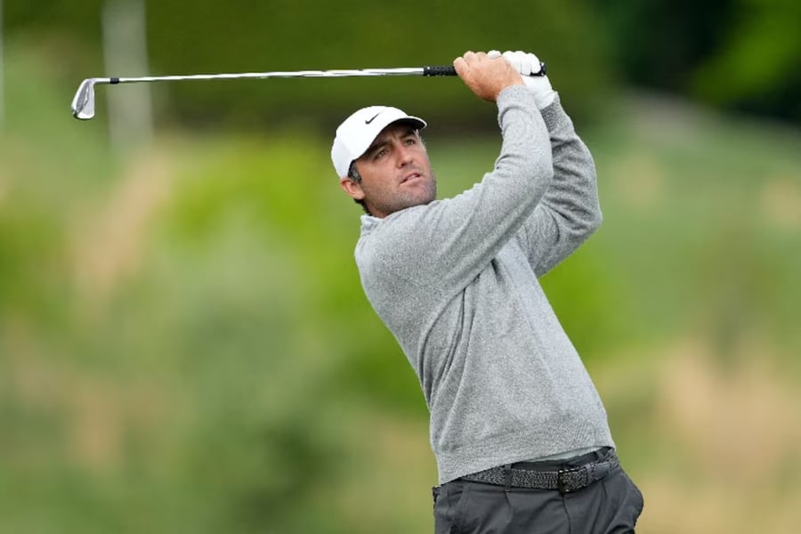 Scottie Scheffler walking on fairway during PGA Championship 2026 at Aronimink with crowded leaderboard in background