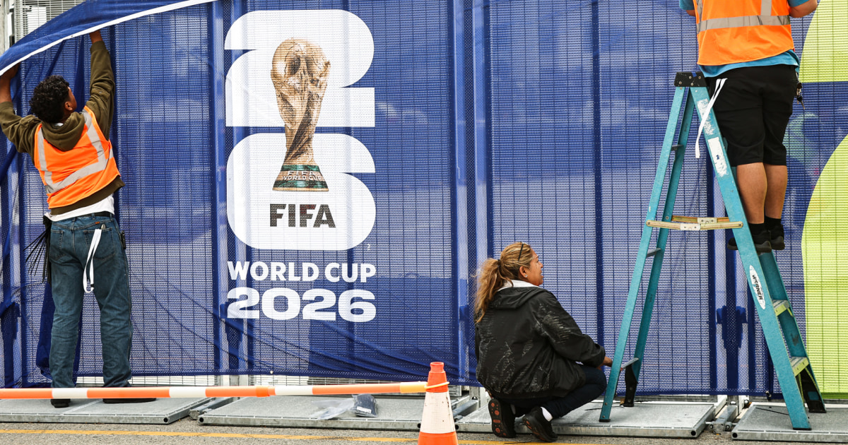 Workers affixing FIFA World Cup 2026 logos on fencing outside SoFi Stadium in Inglewood California