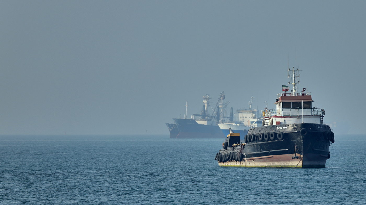 An Iranian tugboat in the Strait of Hormuz as cargo ships sit at anchor, May 4, 2026, illustrating the global shipping disruption at the center of US-Iran nuclear deal talks