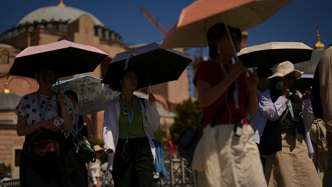 Tourists use umbrellas to shield themselves from intense sun outside Istanbul's Hagia Sophia during a summer 2025 heatwave