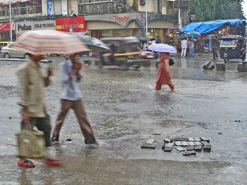 A Mumbai street under monsoon rain and grey skies