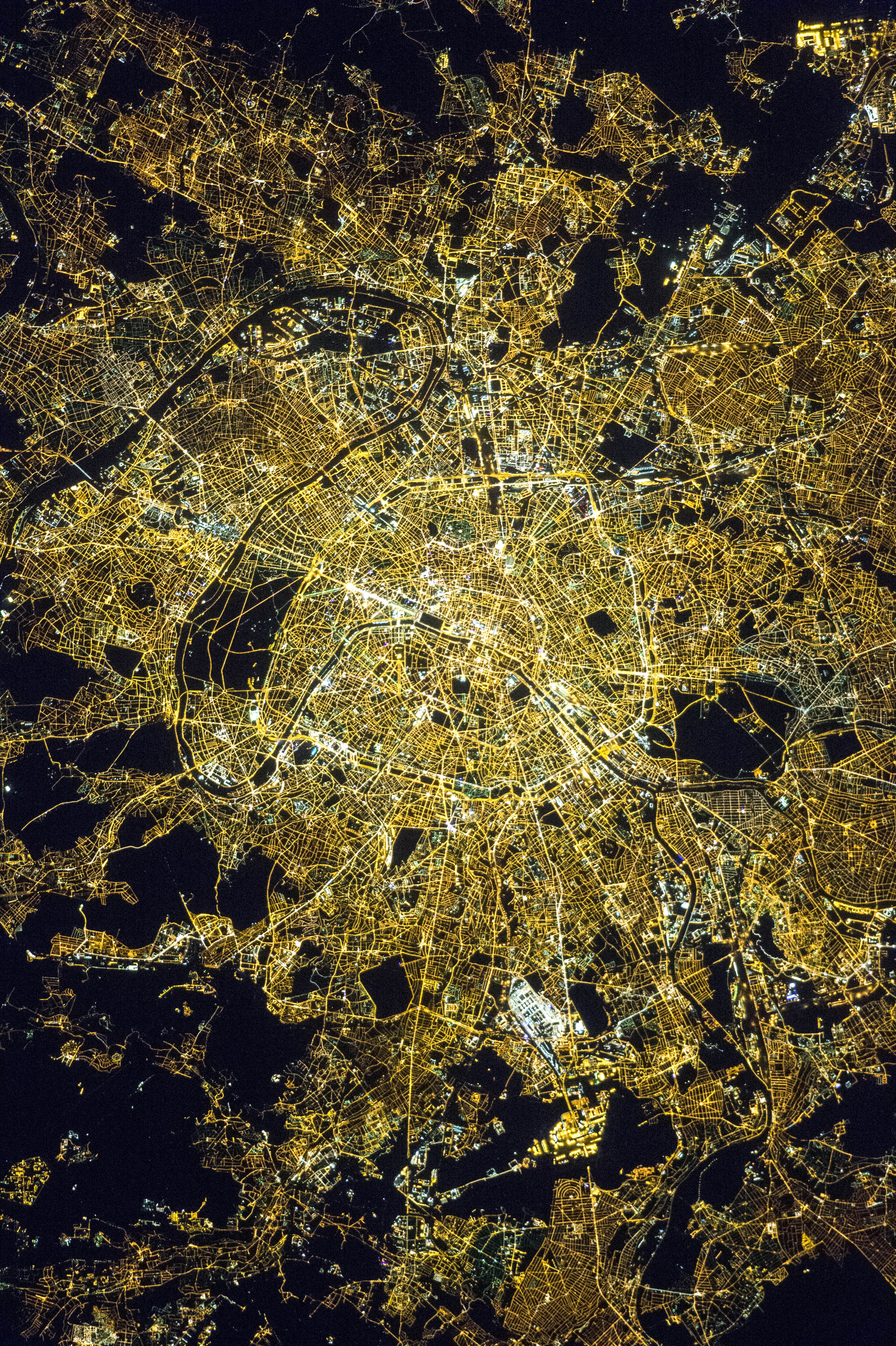 NASA astronaut photograph of Paris at night showing the Seine River as a thin black line with the bright Avenue des Champs Elysees and the radial street pattern around the Arc de Triomphe