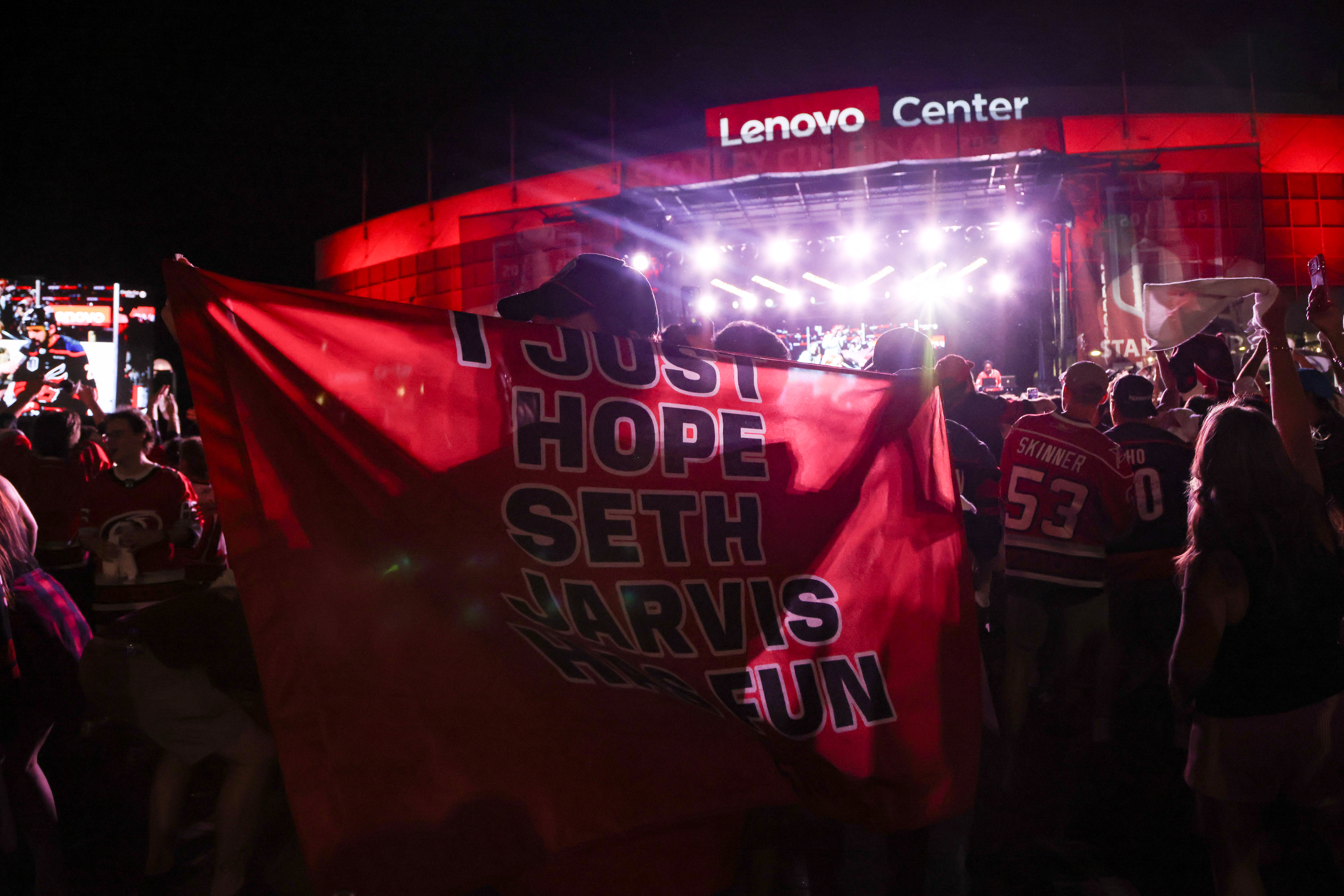 A fan holds a cape reading 'I just hope Seth Jarvis has fun' in the crowd at Lenovo Center during Game 2 of the 2026 Stanley Cup Final