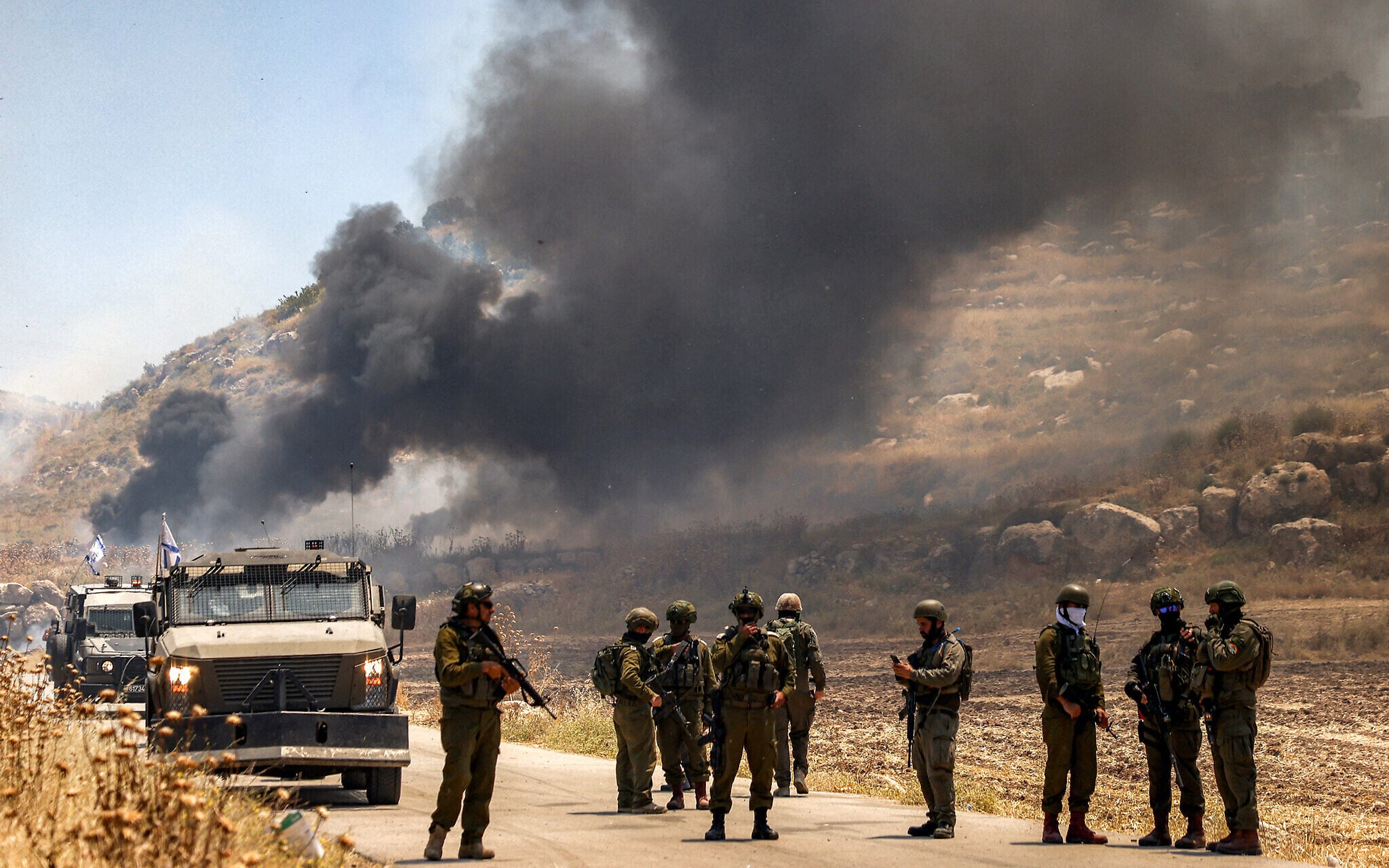 Israeli security forces stand guard as smoke billows from area set ablaze by settlers in Palestinian village of Idna near Hebron