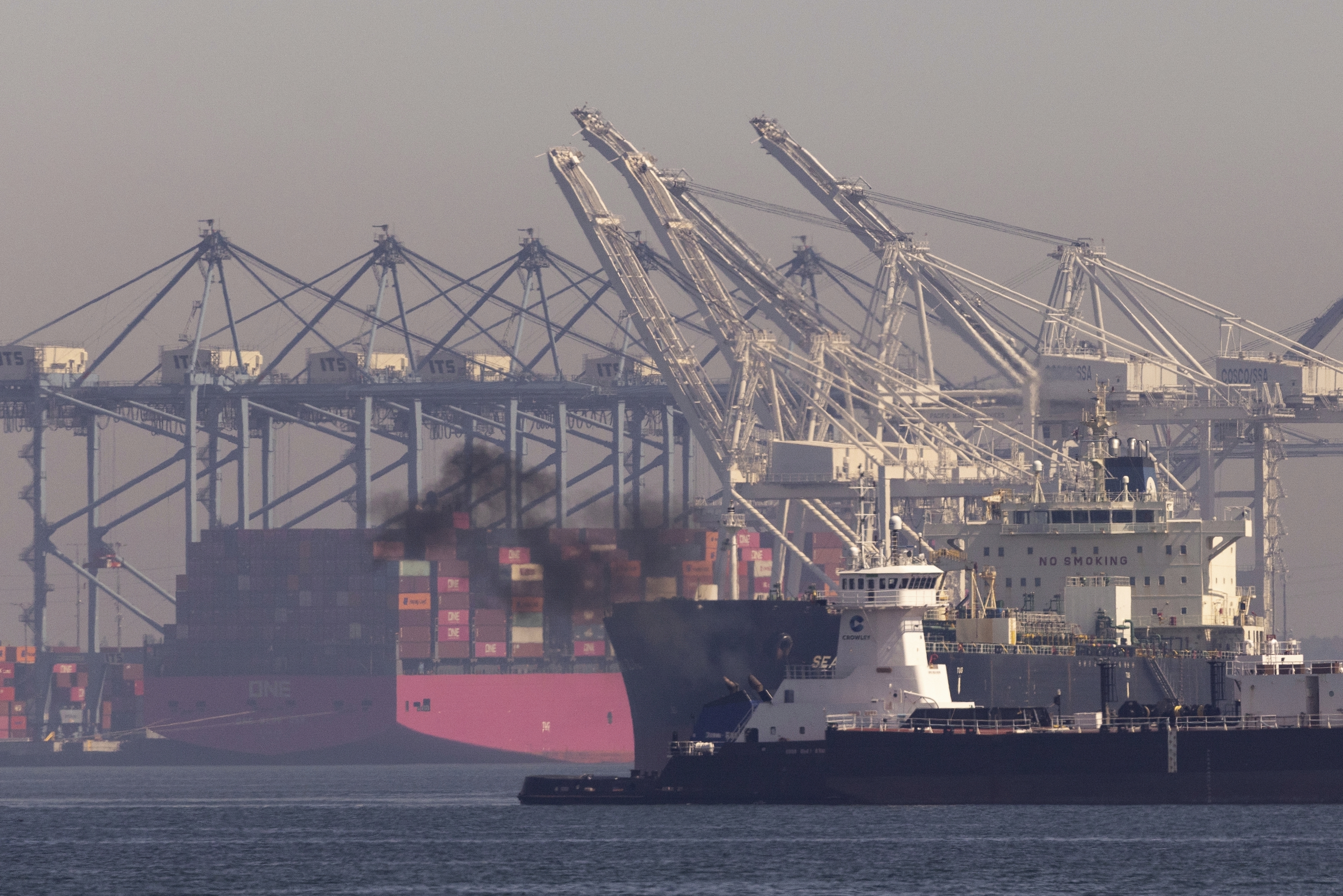 Pollution rises from a ship cruising past the Port of Long Beach in San Pedro, California, where tankers and container ships enter and exit