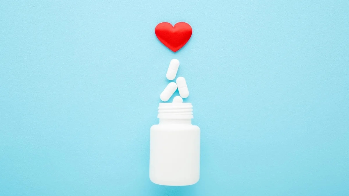 Heart medication pills spilling from bottle on blue background
