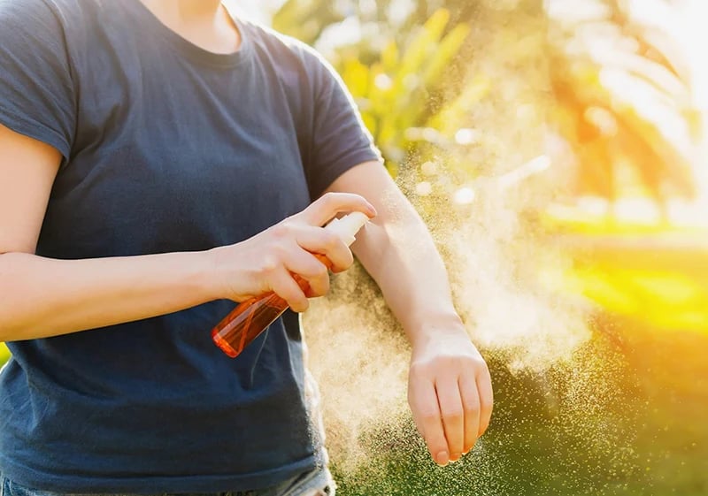 Person applying DEET insect repellent to arm to prevent tick bites outdoors