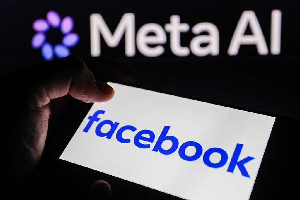 Hand holding smartphone displaying Facebook logo with Meta AI logo in the background