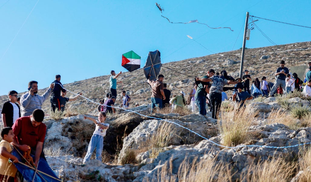 Palestinians and solidarity activists fly kites with Palestinian flag colors in Burin village, West Bank, toward the Israeli settlement of Har Bracha