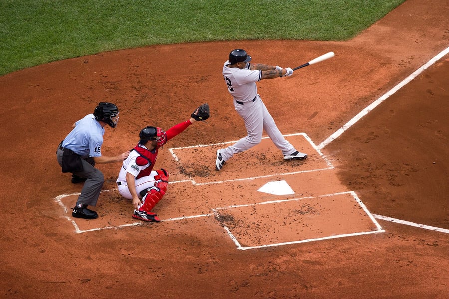 Overhead view of a baseball batter completing his swing at home plate as the catcher and home plate umpire crouch behind him