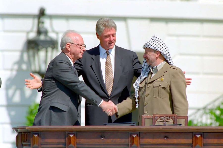Yitzhak Rabin shaking hands with Yasser Arafat as Bill Clinton stands between them with arms outstretched on the White House lawn