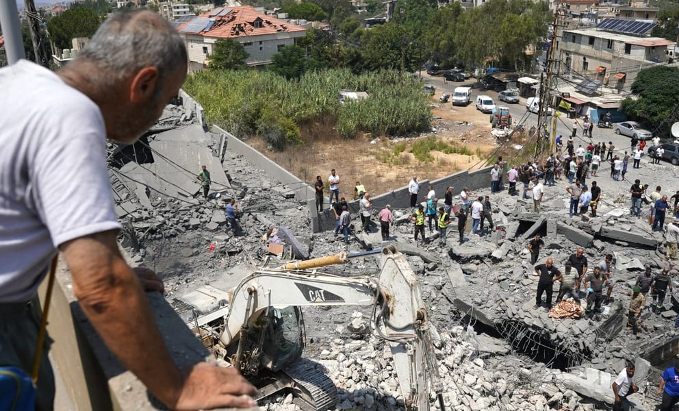 A man watches as heavy machinery, first responders and residents search the site of an Israeli airstrike in Deir al-Zahrani, southern Lebanon, on August 15, 2026