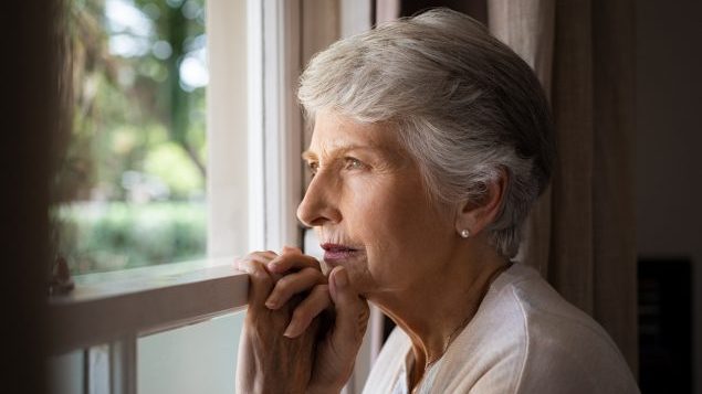 Older woman looking out window representing dementia and Alzheimer's disease risk in aging adults