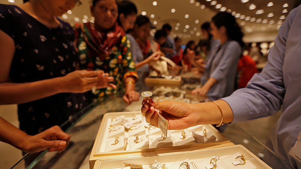 A jeweller shows a gold ring to customers in India as the gold rate today reaches Rs 16,309 a gram for 24K