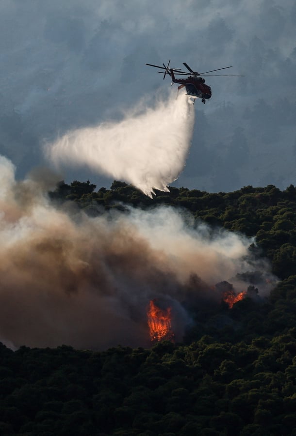 Firefighting helicopter drops water over wildfire smoke billowing near Porto Germeno resort along the Gulf of Corinth in Greece, August 2026
