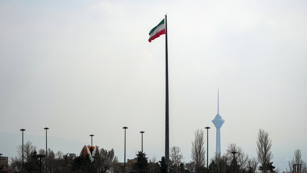 Iranian national flag flies over Tehran skyline with Milad Tower amid US sanctions and Strait of Hormuz oil cutoff threat