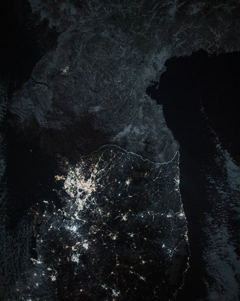 NASA International Space Station photo of the Korean Peninsula at night showing the stark contrast between brightly lit South Korea and almost entirely dark North Korea, with only Pyongyang visible