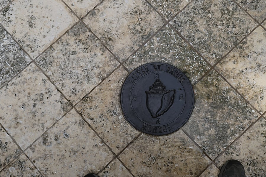 A circular bronze marker set into stone tiles reading Little St James with cardinal directions and the date MCMXCI