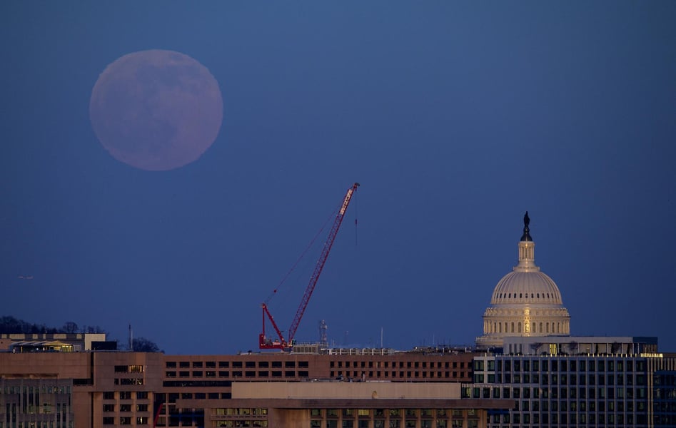 A near-full moon rising in deep blue twilight above the dome of the United States Capitol