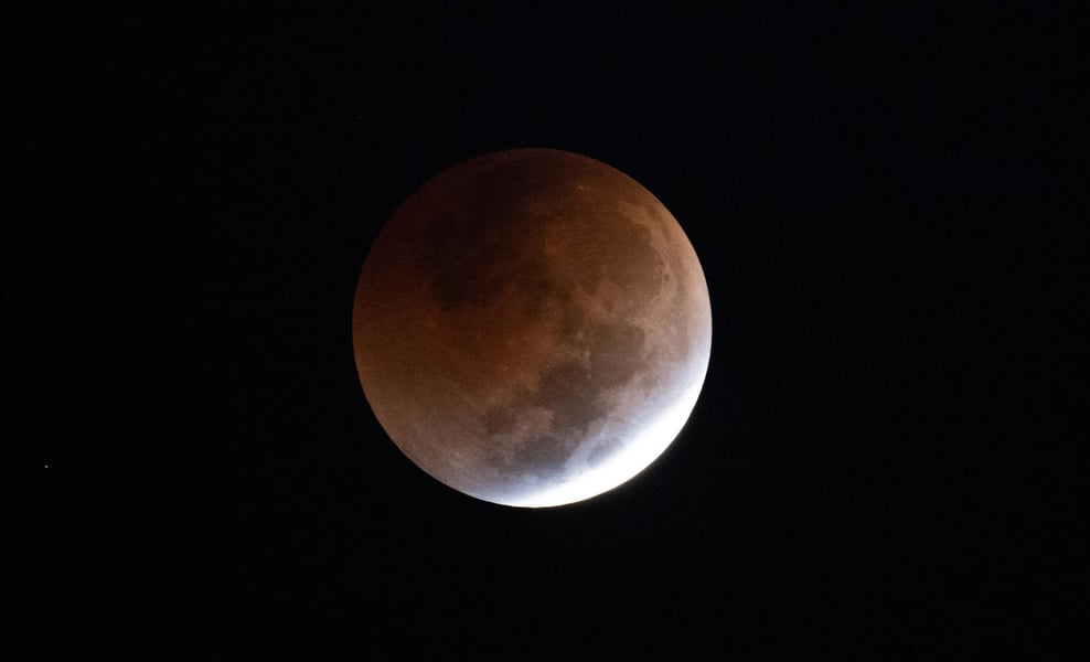A moon almost entirely inside the Earth’s umbra, coppery, with one bright uneclipsed sliver on the lower limb