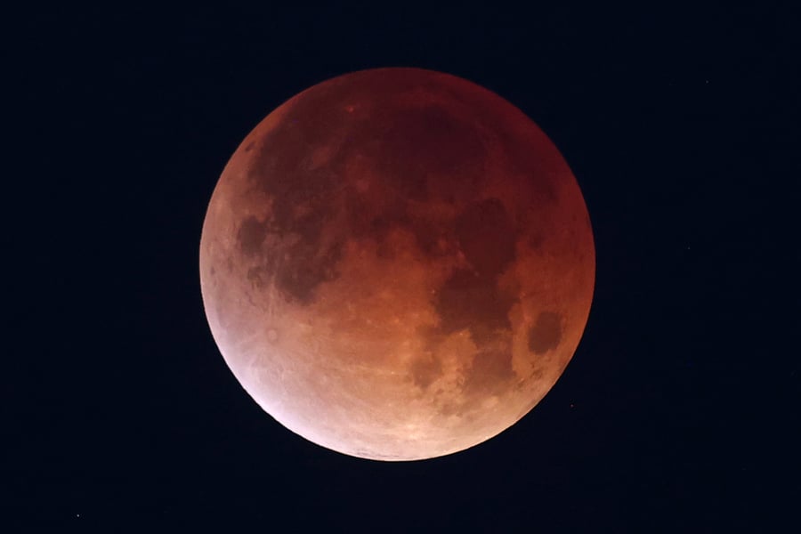 A totally eclipsed moon glowing deep copper red against a black sky