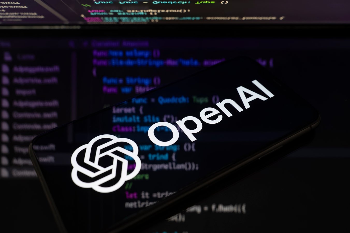 OpenAI logo displayed on a smartphone screen with lines of code projected onto a reflective surface