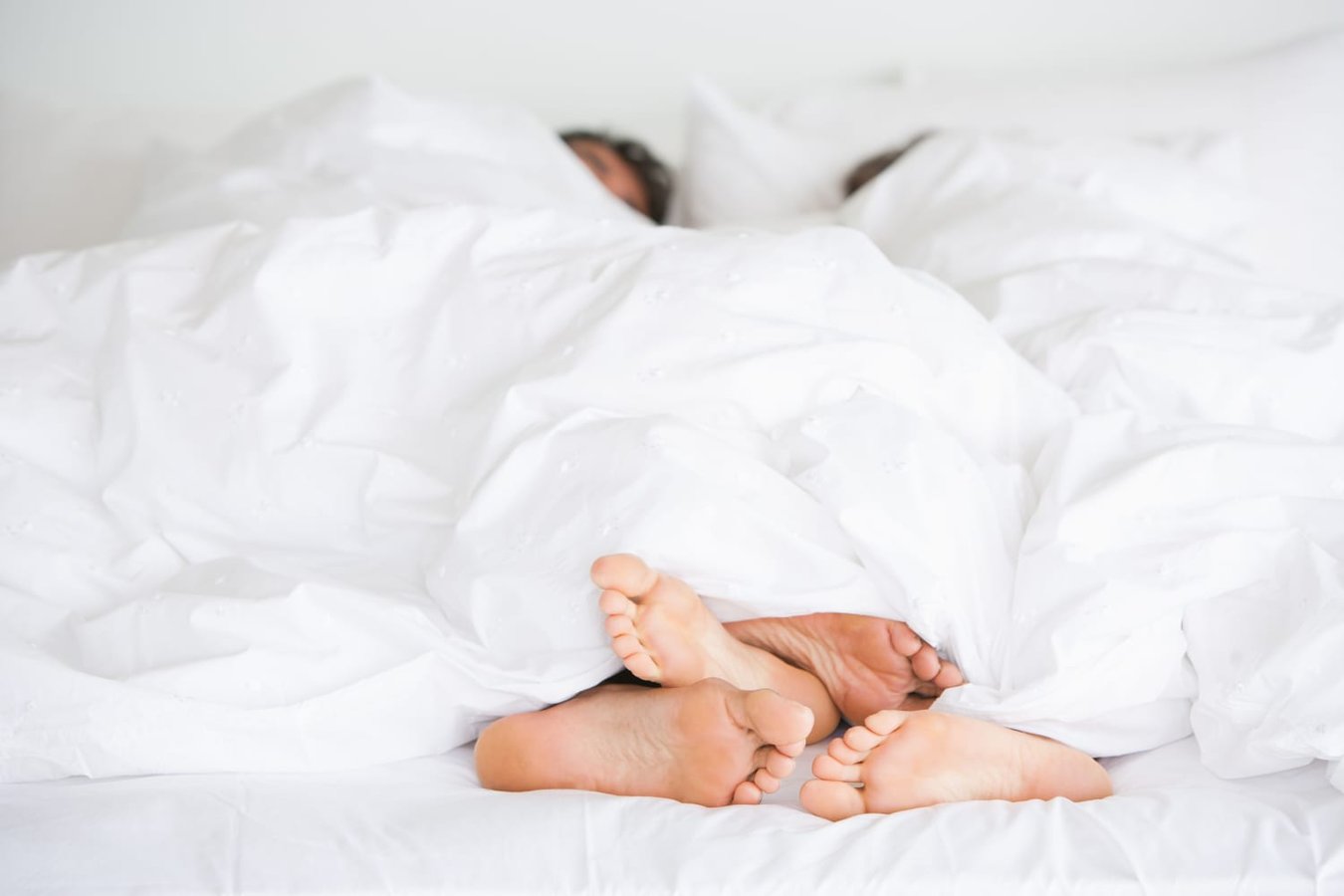 Couple's feet in bed illustrating research on sex frequency and relationship happiness