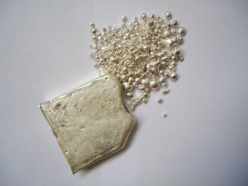 Today silver price: a rough cast silver ingot beside scattered silver casting granules on a white surface