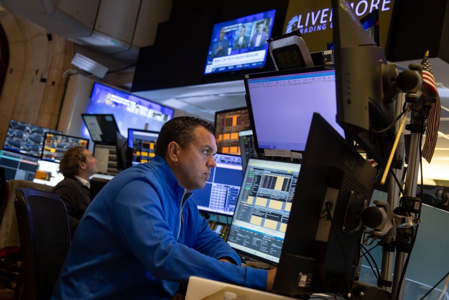 S&P 500 futures today: a trader works at a multi-screen dealing desk beneath a television carrying a megacap technology headline
