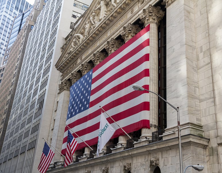 The New York Stock Exchange facade on Wall Street draped with a large United States flag between the Corinthian columns